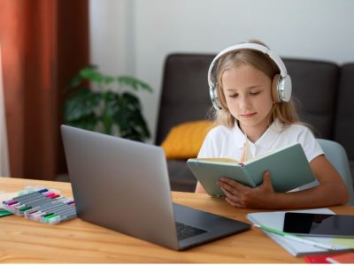 Момиче с лаптоп и книга по време на онлайн курс по английски език